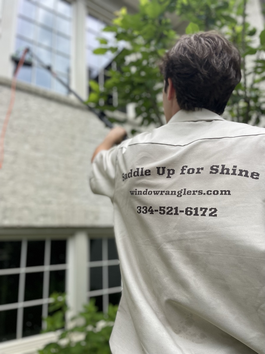Window Wranglers crew member cleaning second-story windows of a brick Auburn, AL home with a water-fed pole